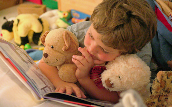 Immagine di un bambino che legge un libro assieme a dei peluches.